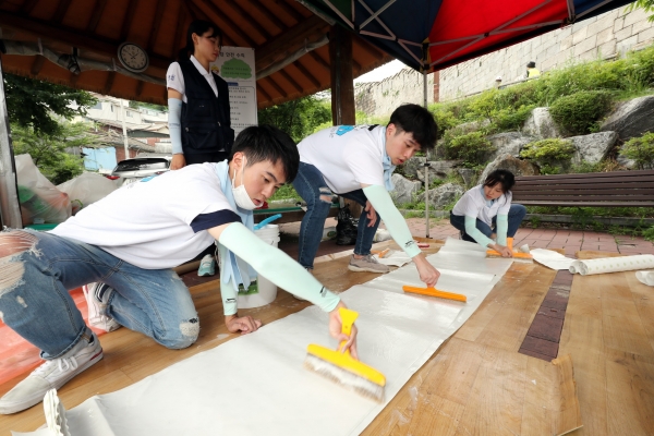 대우건설 대학생 홍보대사들이 서울시 성북구에 위치한 노후주택에 도배할 벽지에 풀을 바르고 있다. (사진=대우건설)