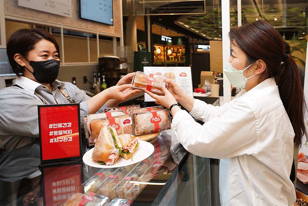 신세계푸드가 위탁운영 중인 서울 중구 을지로 SKT타워 지하 구내식당에서 한 여성한테 대체육 샌드위치를 건네주고 있다. (사진=신세계푸드)  